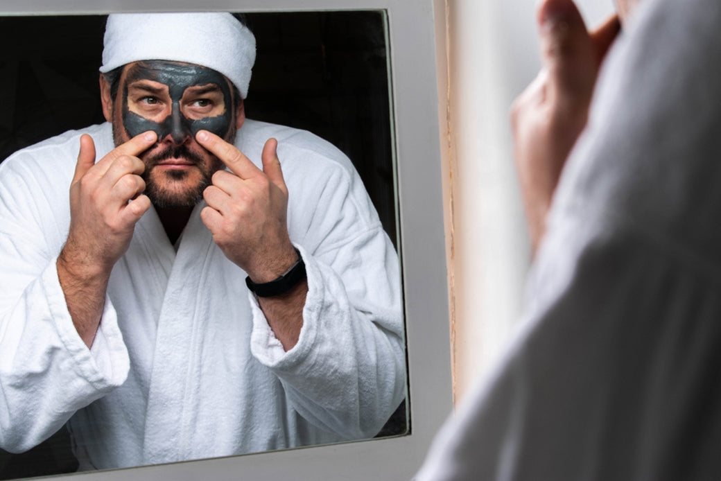 a man in a robe applying a charcoal clay skin detox mask